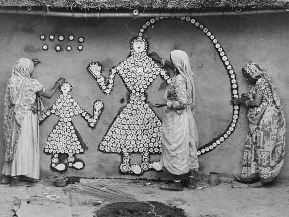Black and white photograph of women painting figures on a wall.