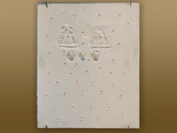 White rectangular plaster sculpture with impressions of triangles and Egyptian motifs