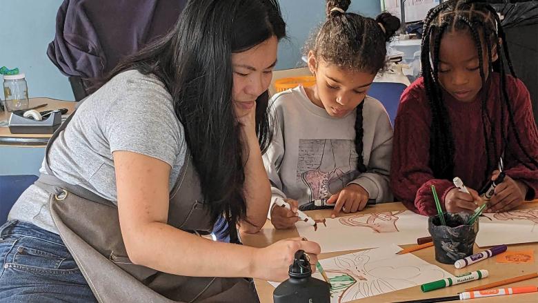 An adult and two children sit at a table and draw.