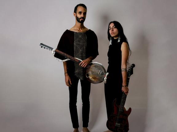 Musicians Jake Blount and Mali Obomsawin stand with stringed instruments and pose for the camera. 