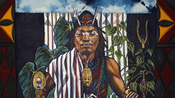 Detail of painting and textile on wood; an enthroned male figure faces out, wears black-and-white striped garment. Green plants around with emblems of Eze Nri