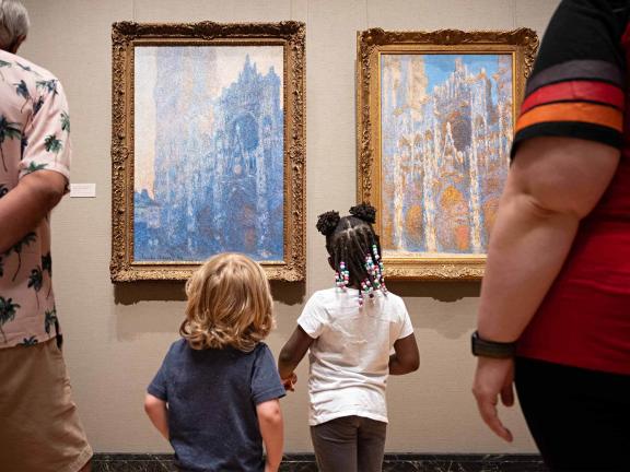 Two children stand in front of two paintings from Monet's Roulin Cathedral series.