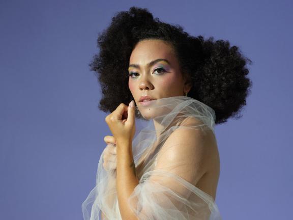 Musician Madison McFerrin poses wrapped in a tulle fabric and donning colorful eye makeup.