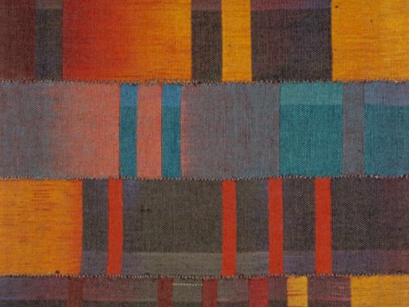 A photograph of cotton dyed with the colors of orange, teal, red, and brown woven together.