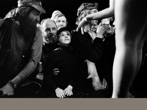 Black and white photo of young boy and other people in a crowd at a performance. 