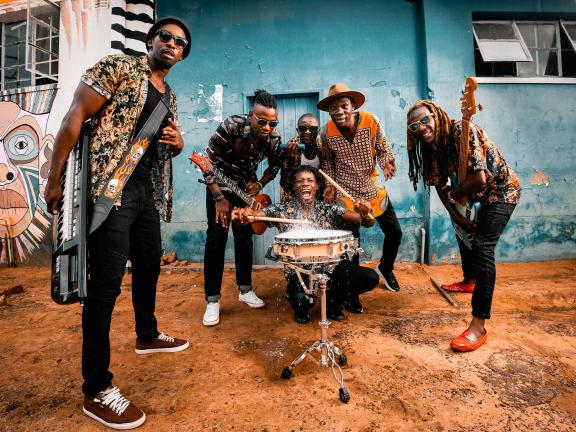 The band Mokoomba poses for the camera while carrying and playing various instruments. 