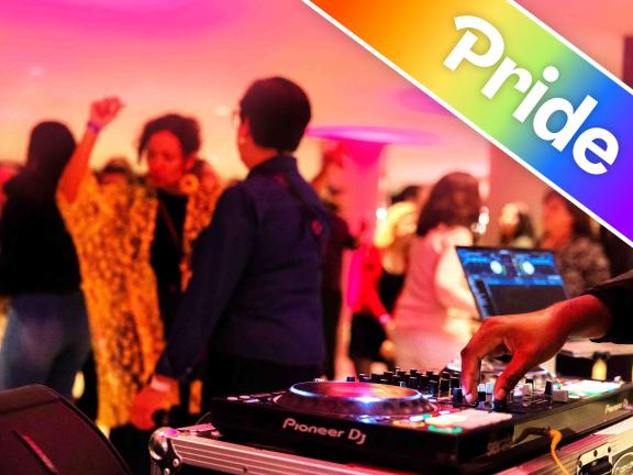 People dance in a dimly lit room while a DJ spins records.