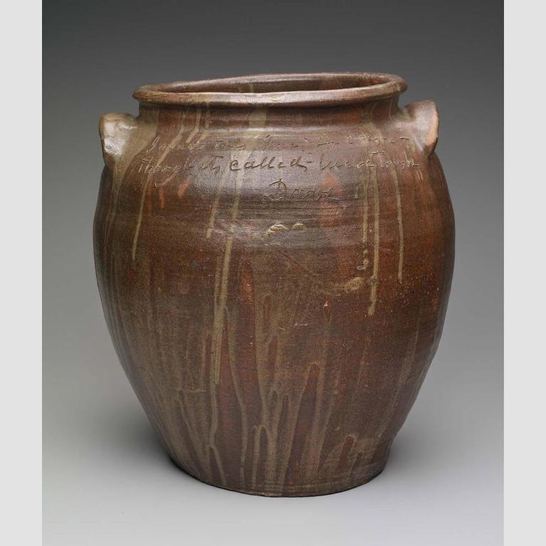 A brown clay pot with a lip, two handles, and dripped in a lighter glaze.