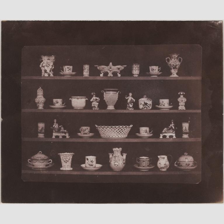A photo of various china vases, cups, and trinkets displayed on four shelves.