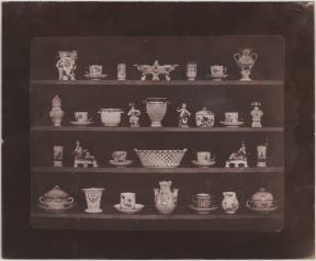 A photo of various china vases, cups, and trinkets displayed on four shelves.