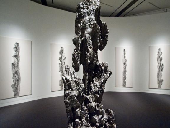 scholar's rock sculpture in gallery with four paintings of the rock on the wall behind it