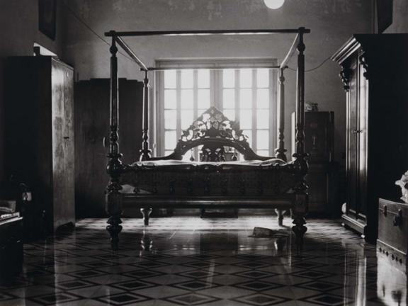 An empty, wooden bed sits in a room with other wooden furniture. 