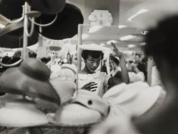 A woman looks in a department store mirror as she tries on a hat for sale.