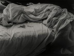 A black-and-white photo of bobby pins sitting atop an unmade bed. 