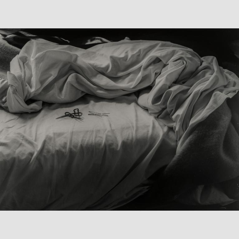 A black-and-white photo of bobby pins sitting atop an unmade bed.