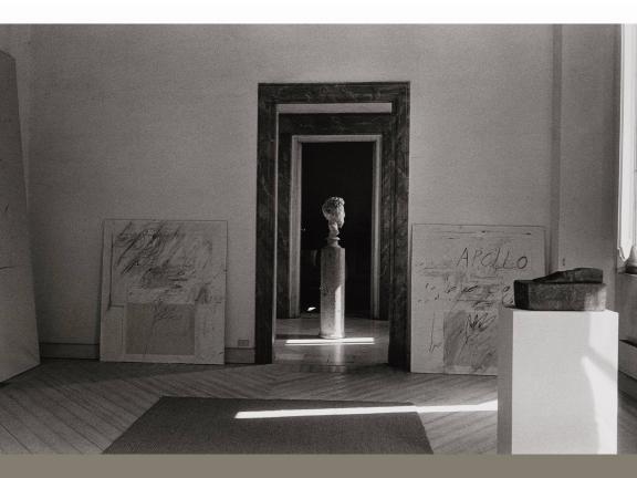Black-and-white photograph of a bust resting on a column in between two doorways. 