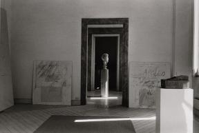 A bust on a pedestal seen through a door frame.