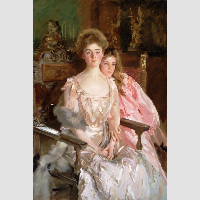 A woman and her daughter wear flowing gowns and sit close to one another on ornate chairs.