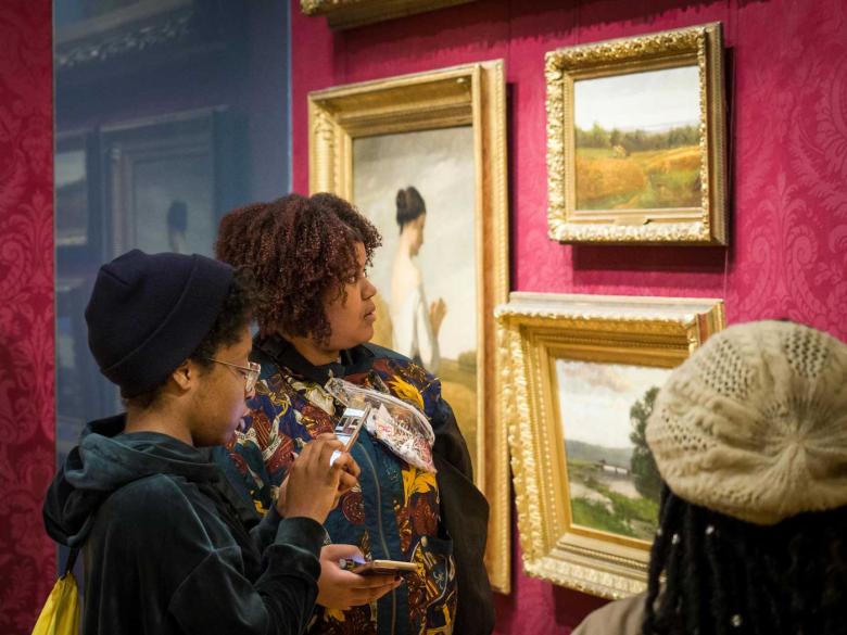 Two visitors holding smartphones looking at paintings in Salon gallery