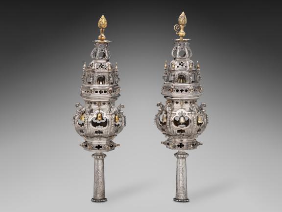 A photo of a pair of silver and gold Torah finials intricately decorated with star and flower cutouts, bells, etchings, and more.