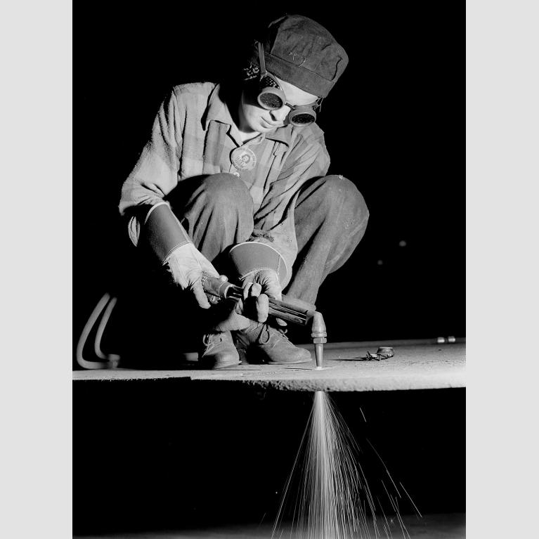 Flame burner Ann Zarick welding a sheet of metal.