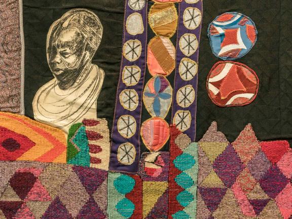 A hanging, mixed textile media, rectangular banner with tassels that depicts different shapes and figures. 