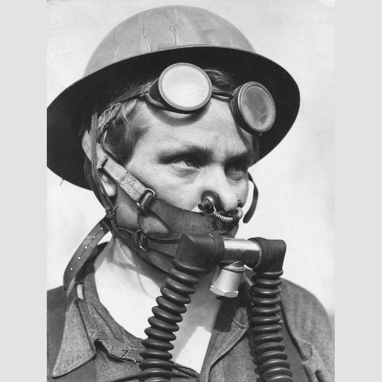 A woman, Bernice Daunora, wears a helmet, goggles on her forehead, and a breathing apparatus that covers her nose and mouth.