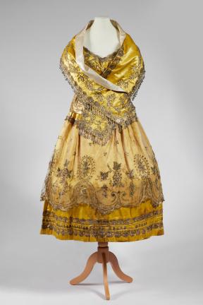 A yellow, beaded dress and scarf combination placed on a mannequin. 