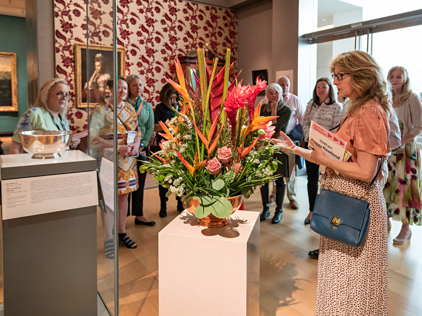 A tour guide and visitors in front of large floral arrangement