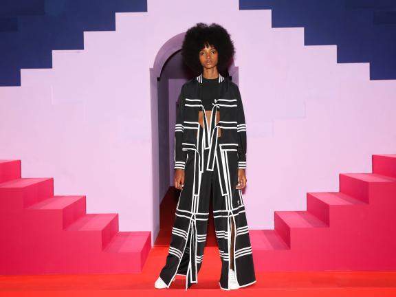 A model wears an Adidas outfit and stands against a bright, abstract set. 