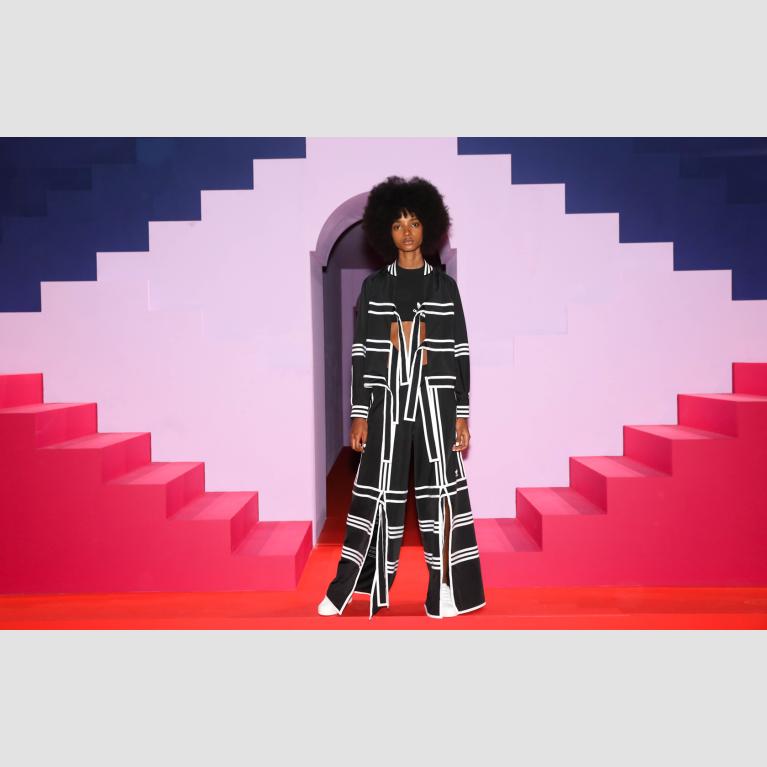 A model wears an Adidas outfit and stands against a bright, abstract tracksuit.