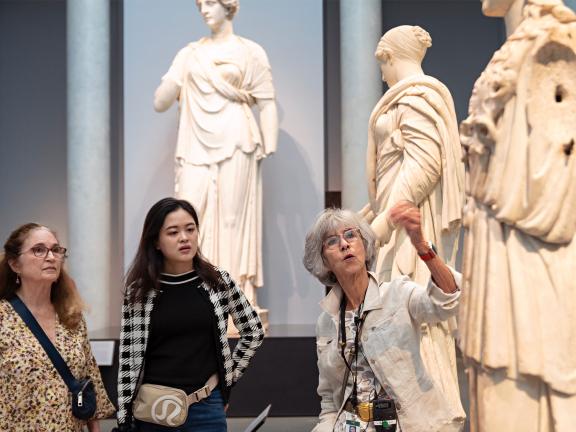 An MFA tour guide gestures toward a statue in the Gods and Goddesses gallery. 