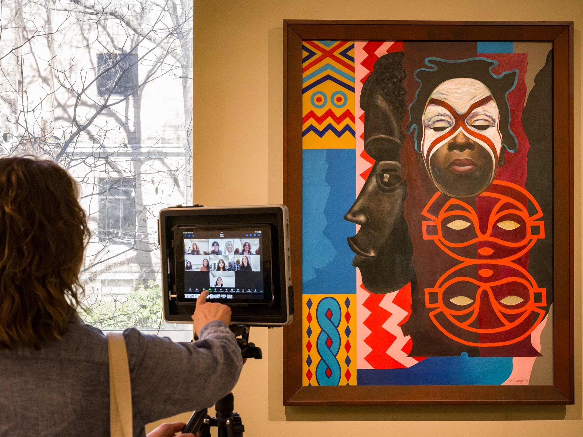 An MFA instructor operating a camera on a tripod pointed at painting on gallery wall