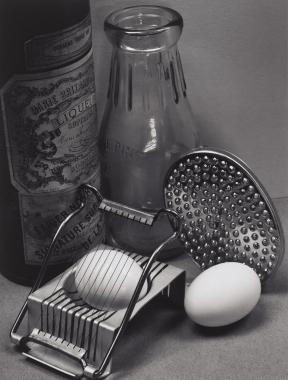 A photo of two hard boiled eggs, one in an egg slicer, next to two bottles.