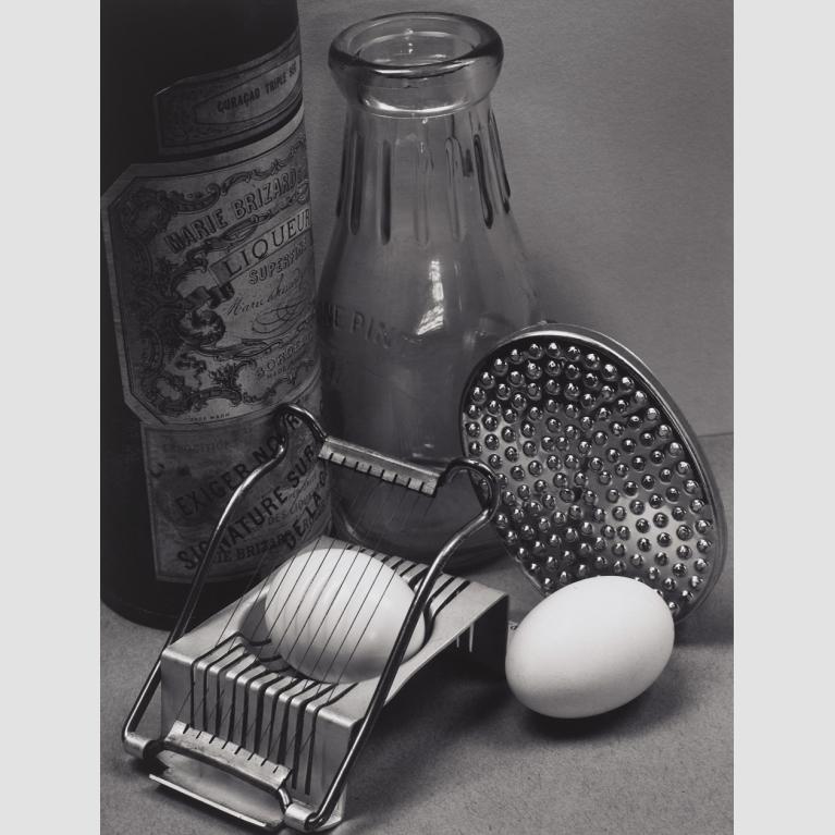 A photo of two hard boiled eggs, one in an egg slicer, next to two bottles.