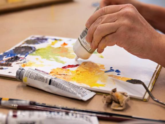 Adult student applies yellow paint to palette (SAC)