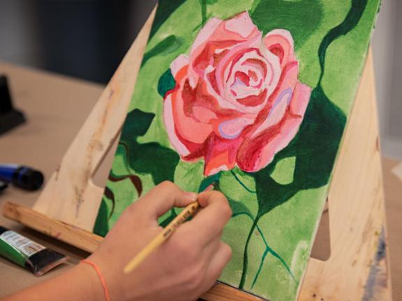Adult student paints pink rose on table top easel (SAC)